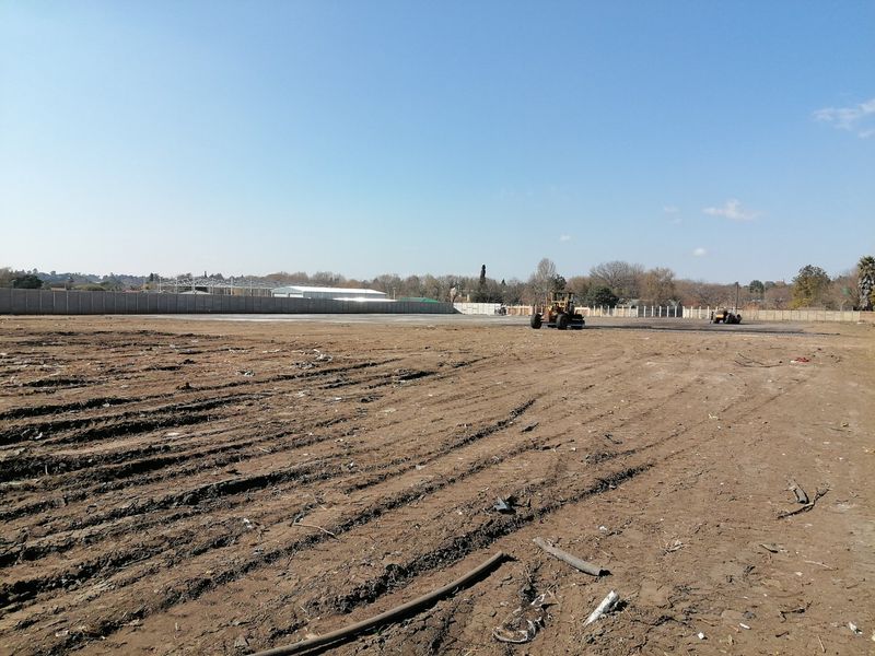 A large, cleared residential vacant land plot featuring a perimeter precast concrete boundary wall and ongoing site preparation work.