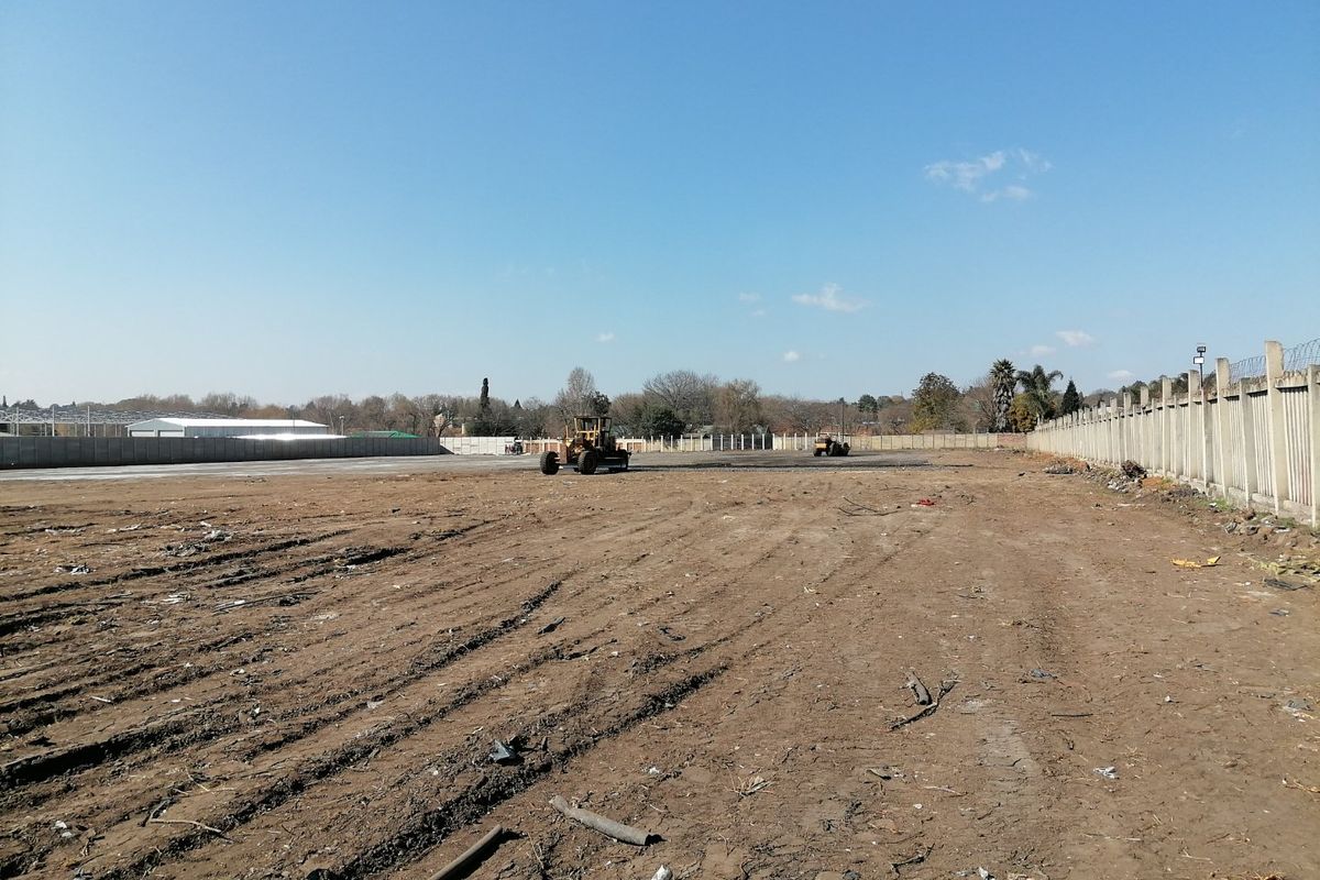 A large, cleared vacant residential plot featuring a perimeter precast concrete boundary wall with security spikes, currently undergoing site preparation.