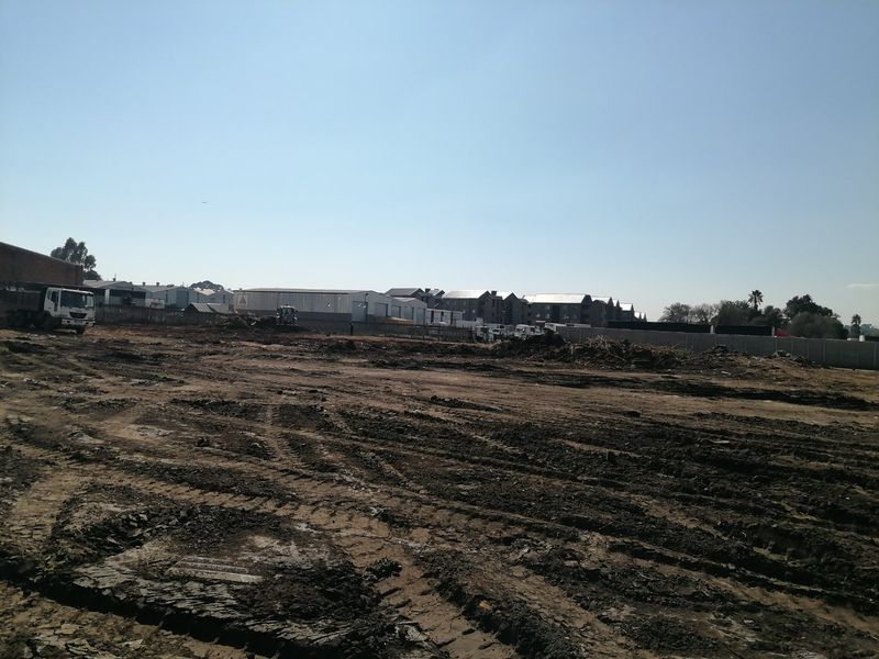 A wide view of a vacant residential plot showing cleared earth and boundary walls, ready for development.