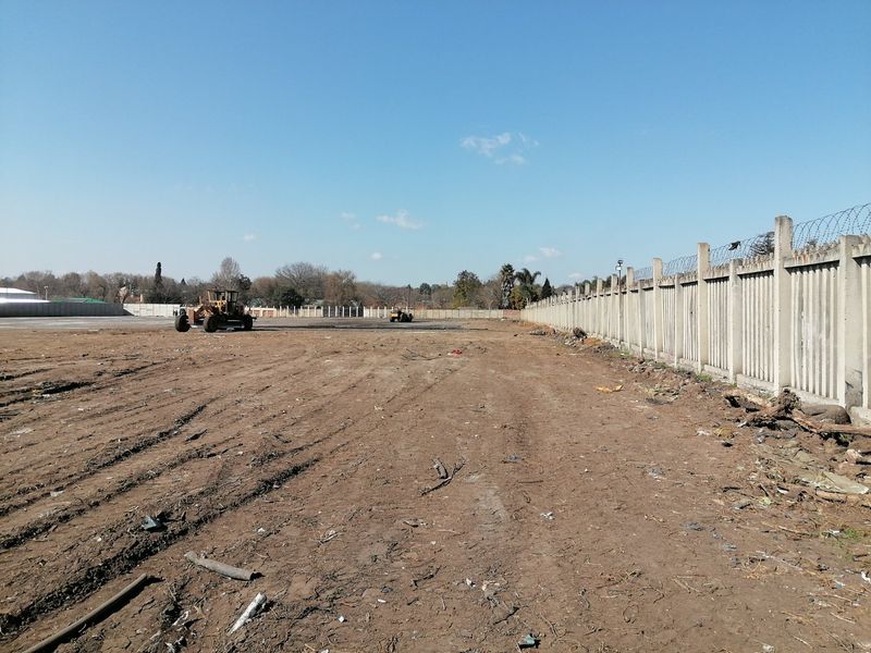 A vacant residential plot featuring a precast concrete boundary wall with razor wire fencing and cleared earth.