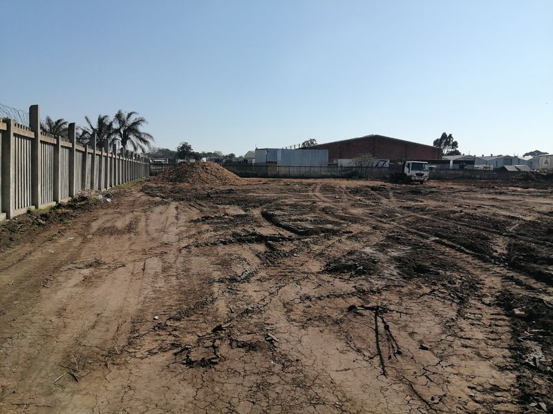 A vacant residential plot featuring cleared earth, perimeter precast concrete walling, and barbed wire fencing, ready for development.
