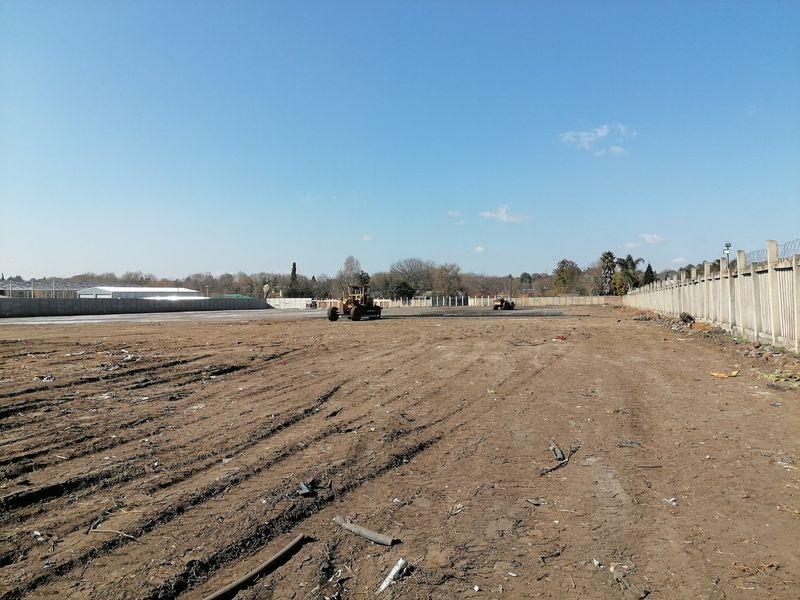 A large, cleared vacant residential plot featuring a perimeter precast concrete boundary wall with security spikes, currently undergoing site preparation.