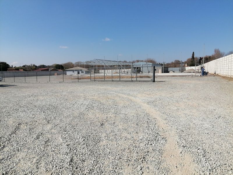 A vacant residential plot featuring a gravel surface, perimeter walling, and an ongoing steel structure construction project.