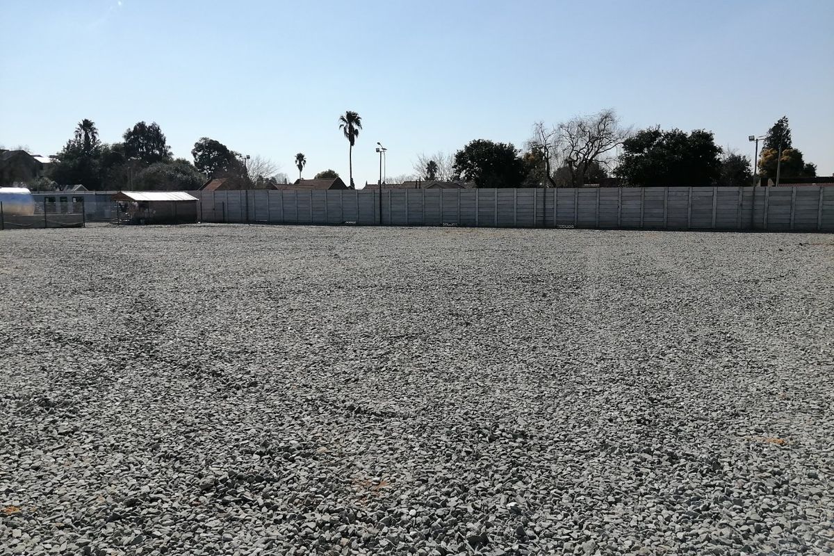 A level, gravel-surfaced vacant residential plot enclosed by a precast concrete perimeter wall, featuring installed floodlights.