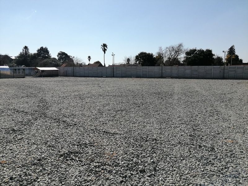 A level, gravel-surfaced vacant residential plot enclosed by a precast concrete perimeter wall, featuring installed floodlights.