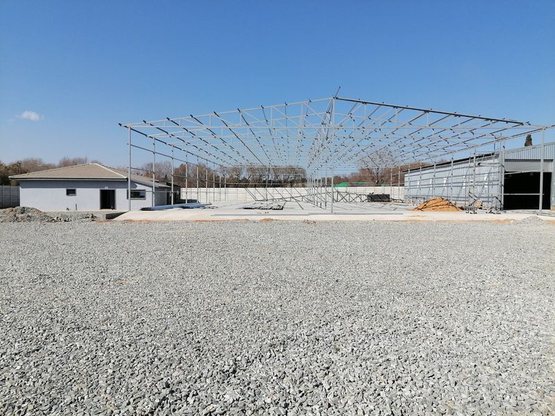 A view of a residential property under construction, featuring a large steel frame structure on a concrete slab with a gravel yard.