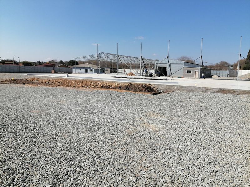 A vacant residential plot featuring a large concrete slab foundation and an ongoing steel frame construction project enclosed by a precast boundary wall.