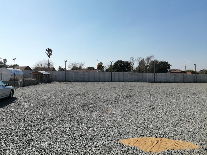 A level, gravel-surfaced vacant residential plot enclosed by a precast concrete boundary wall, featuring installed floodlights and a water tank.