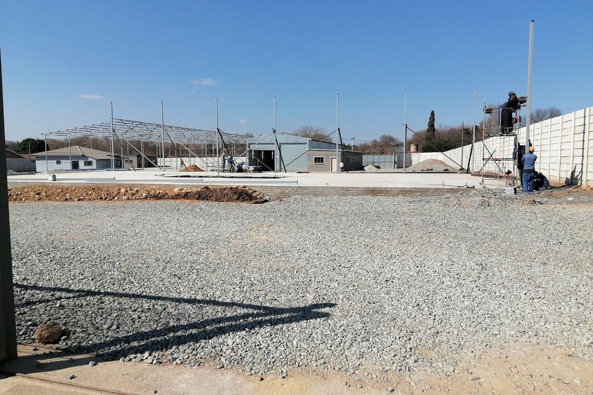 A construction site showing a large concrete slab foundation, steel framework, and perimeter boundary wall under development.