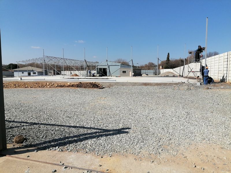 A construction site showing a large concrete slab foundation, steel framework, and perimeter boundary wall under development.