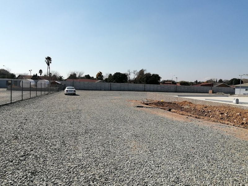 A vacant residential plot featuring a gravel surface, perimeter fencing, and partial brick retaining wall construction.