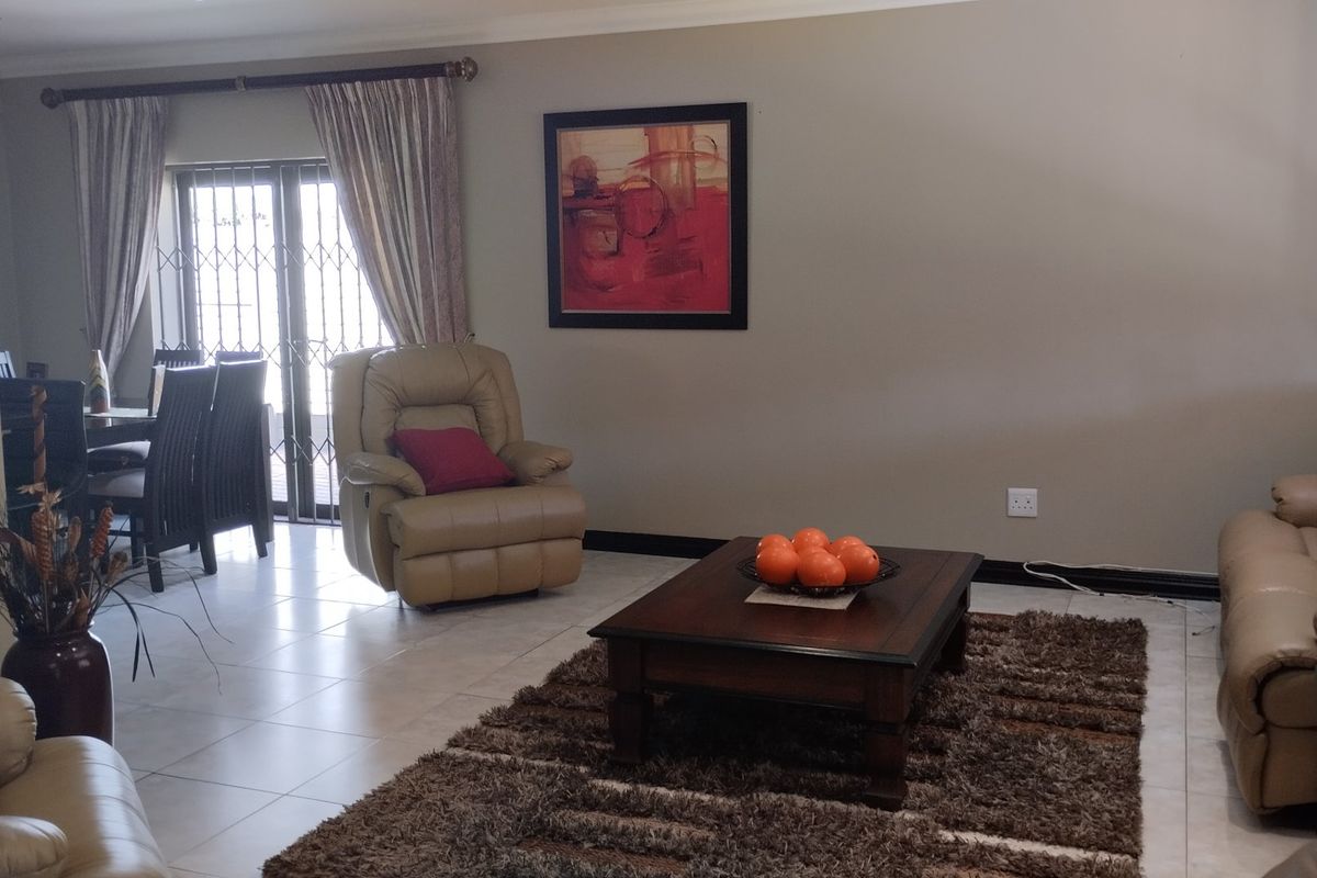 A spacious living room featuring tiled flooring, neutral wall tones, and a sliding door with a security gate leading to the exterior.