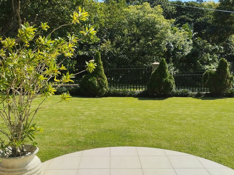A well-maintained private garden featuring a neat lawn, tiled patio area, and secure perimeter fencing with mature greenery.