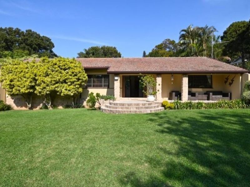 A charming single-story residence featuring a tiled roof, stone-accented pillars, and a welcoming covered patio overlooking a well-maintained front lawn.
