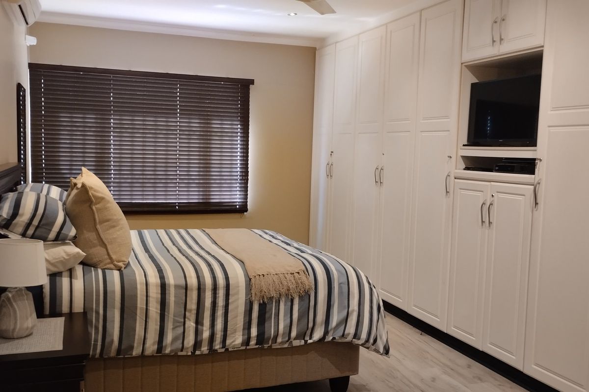 A well-maintained bedroom featuring extensive floor-to-ceiling built-in cabinetry, laminate flooring, venetian blinds, and an integrated air conditioning unit.
