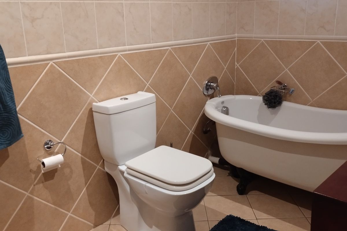 A bathroom featuring a classic clawfoot bathtub and a modern toilet, finished with neutral-toned ceramic wall and floor tiles.