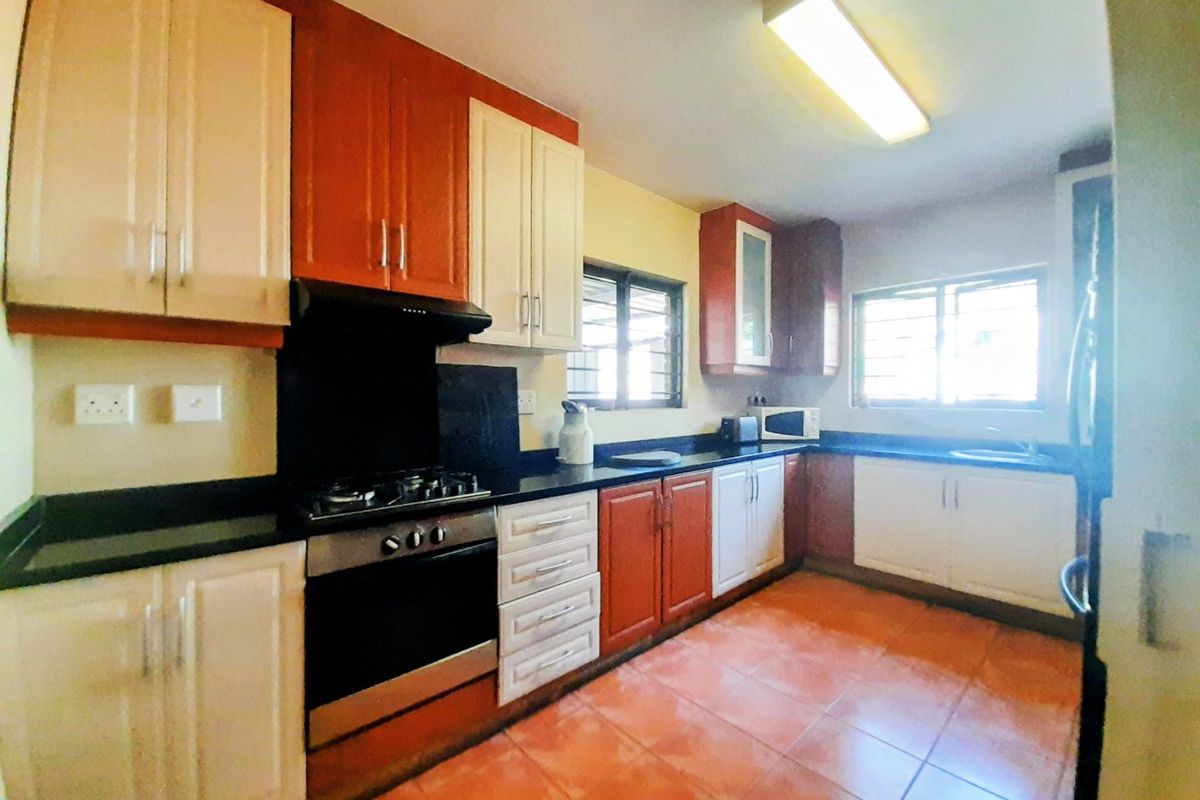A functional kitchen featuring two-tone cabinetry, granite countertops, a gas hob with extractor, and tiled flooring with ample natural light.