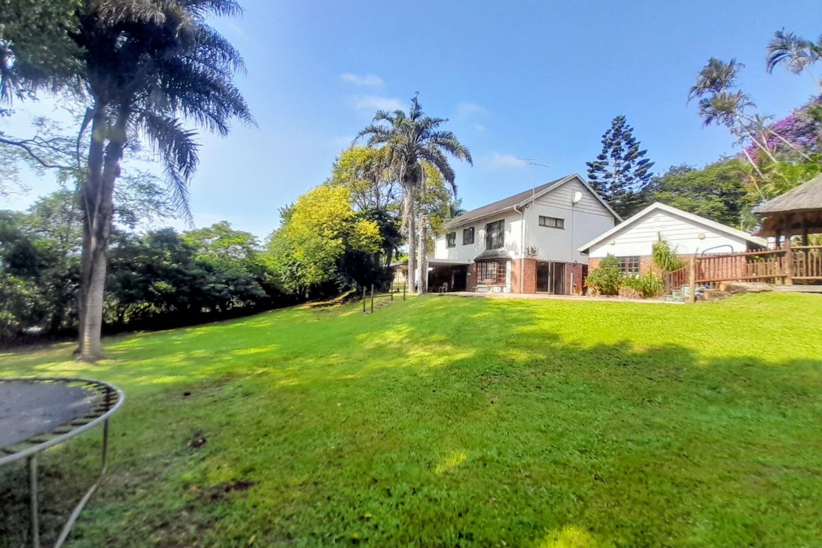 A spacious rear garden featuring a well-maintained lawn, mature trees, and a view of the multi-level residential building with brick and plaster finishes.