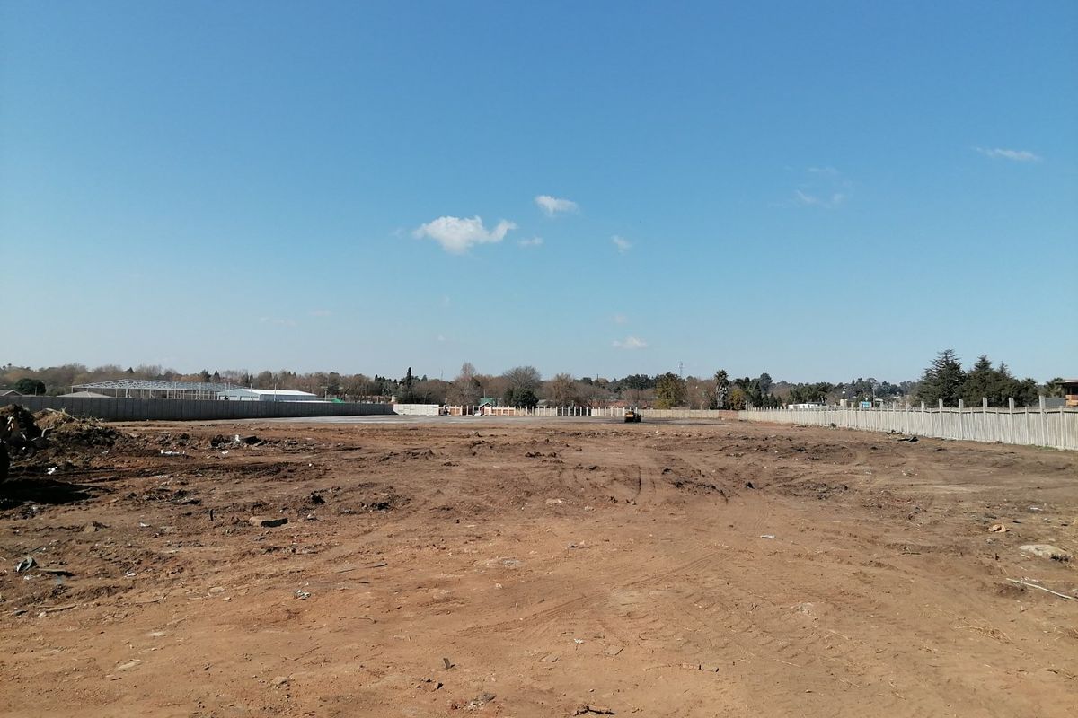 A wide-angle view of a vacant residential plot featuring cleared earth and perimeter precast concrete boundary walls.