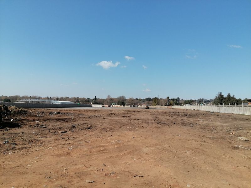 A wide-angle view of a vacant residential plot featuring cleared earth and perimeter precast concrete boundary walls.