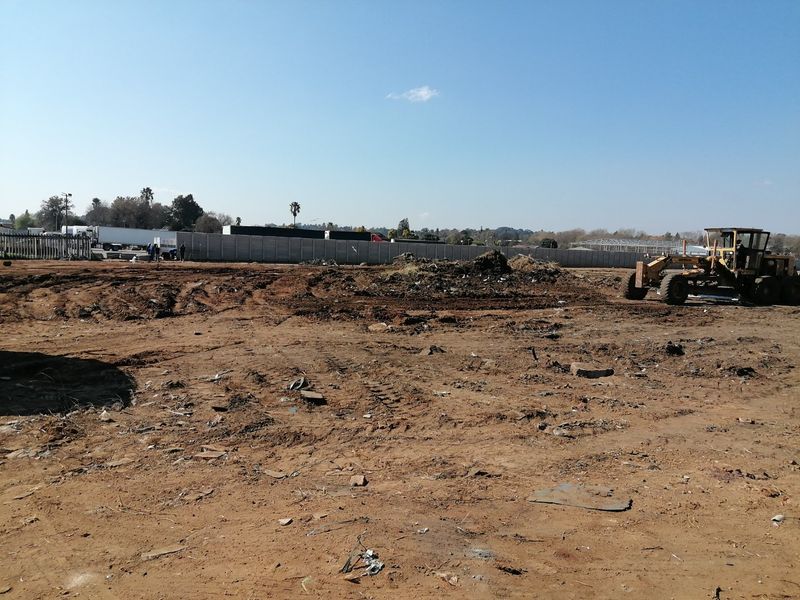 A view of a vacant residential plot showing cleared earth, perimeter walling, and heavy machinery on site.
