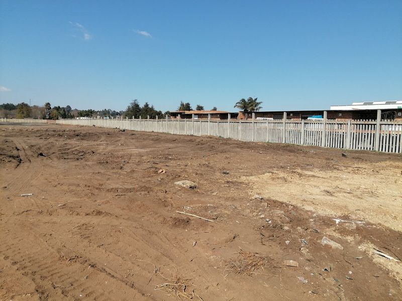 A vacant residential plot featuring cleared earth and a perimeter precast concrete wall with security razor wire.