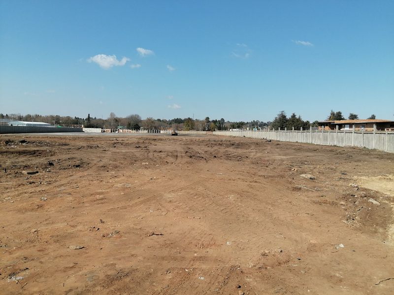 A wide, vacant residential plot featuring cleared earth and concrete perimeter fencing, ready for development.