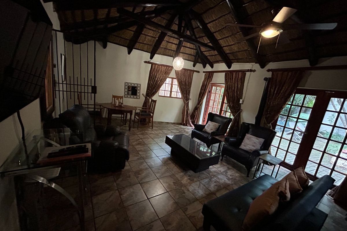 Spacious living area featuring a high vaulted thatched ceiling with exposed timber rafters, tiled flooring, and multiple sets of french doors leading outdoors.