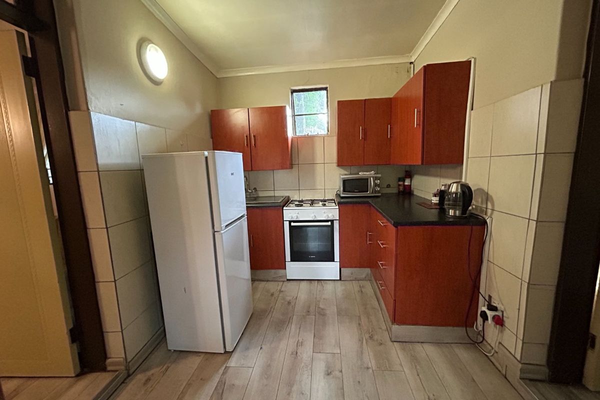 A functional kitchen featuring wood-look cabinetry, tiled splashbacks, laminate flooring, and a freestanding oven and hob.