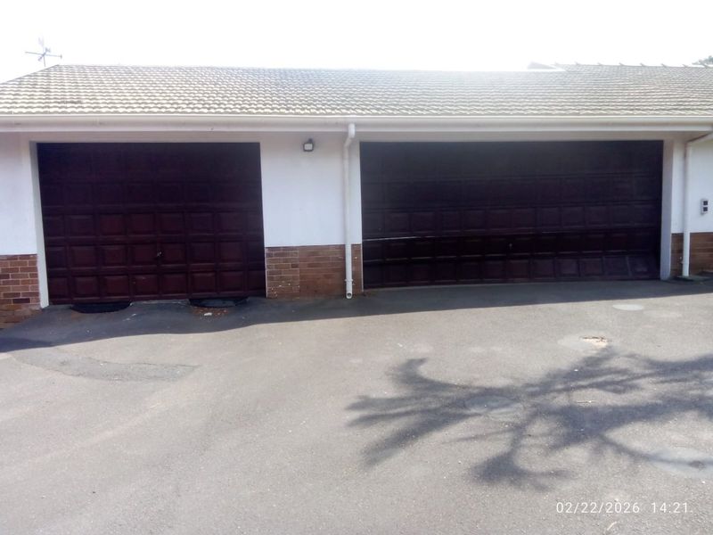 A double garage featuring dark panelled doors, a tiled roof, and a paved driveway area.