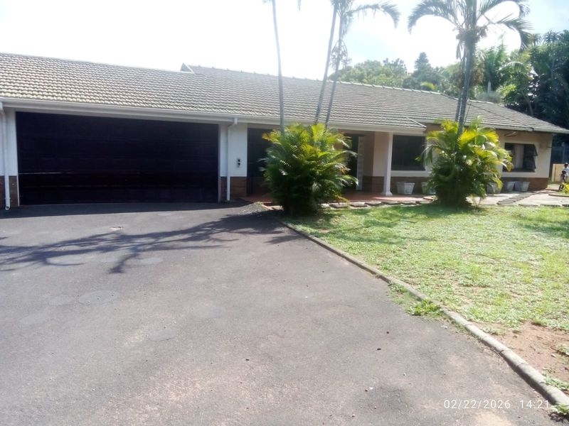 Front elevation of a single-story house featuring a double garage, asphalt driveway, and a covered entrance area with established garden landscaping.