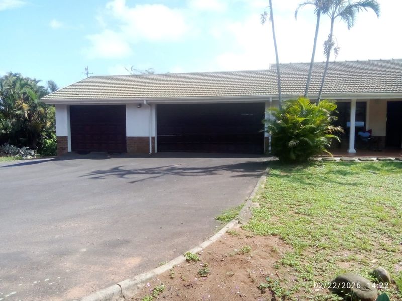 Front exterior view of the property featuring a double garage, tiled roof, and an asphalt driveway with established garden surroundings.