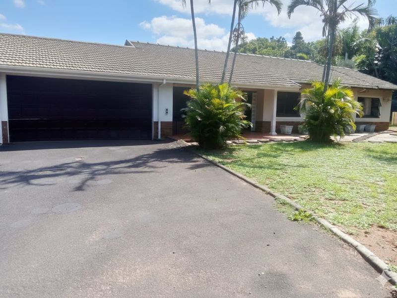 Front elevation of a single-story house featuring a tiled roof, double garage, and an asphalt driveway with established garden landscaping.