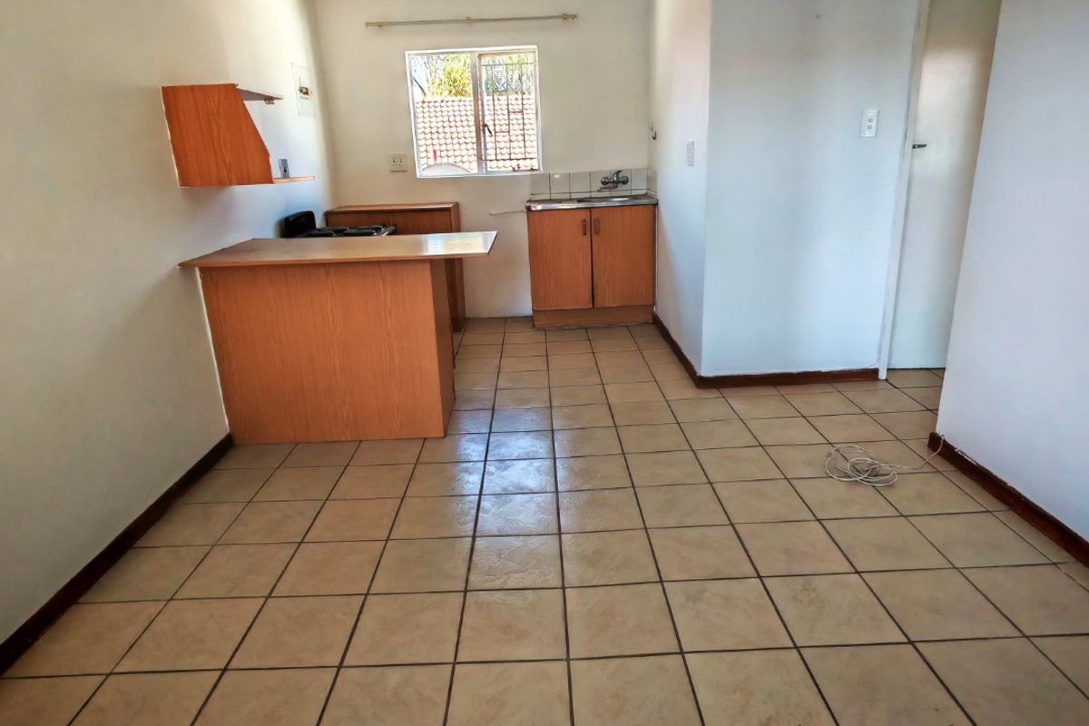 A compact, empty kitchen featuring tiled flooring, built-in wooden cabinetry, and a functional sink area, ready for modernization.