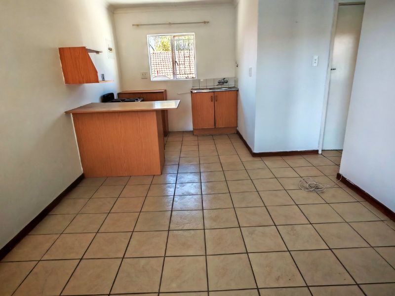 A compact, empty kitchen featuring tiled flooring, built-in wooden cabinetry, and a functional sink area, ready for modernization.