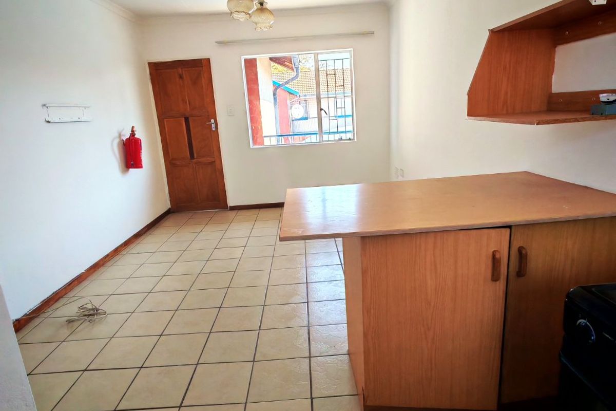 An empty kitchen area featuring tiled flooring, built-in wooden cabinetry with a breakfast counter, and a wall-mounted shelf.