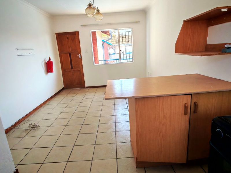 An empty kitchen area featuring tiled flooring, built-in wooden cabinetry with a breakfast counter, and a wall-mounted shelf.
