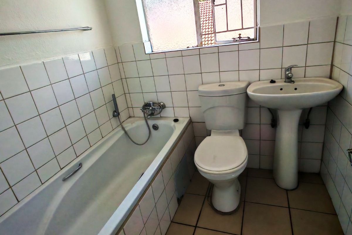 A functional bathroom featuring a standard bathtub, pedestal sink, and toilet with tiled walls and flooring, requiring cosmetic updates.