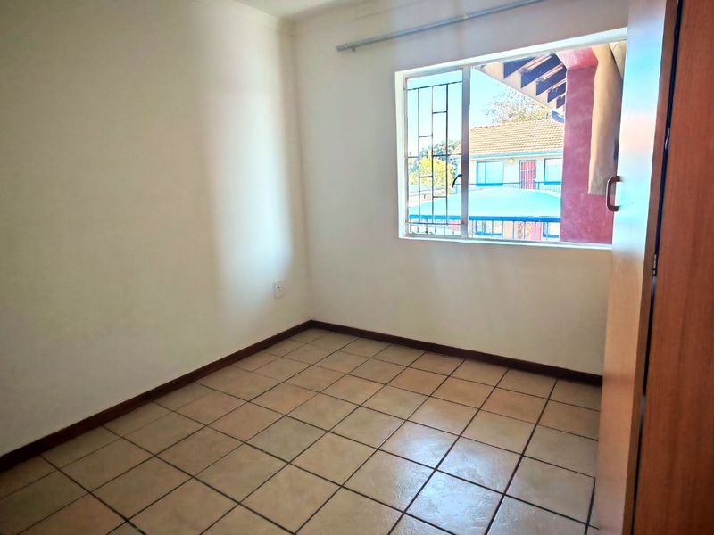 An empty bedroom featuring tiled flooring, a built-in cupboard, and a window fitted with security bars.
