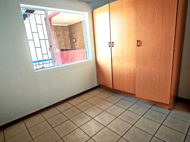 A vacant bedroom featuring tiled flooring, a built-in wooden wardrobe, and a window fitted with security bars.