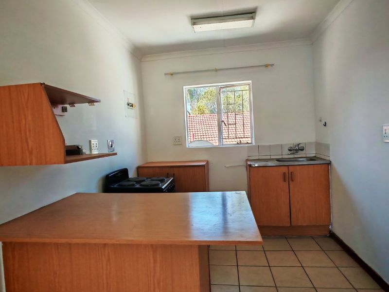 A functional kitchen featuring wood-finish cabinetry, a stainless steel sink, tiled flooring, and a freestanding stove, offering a practical layout for daily use.