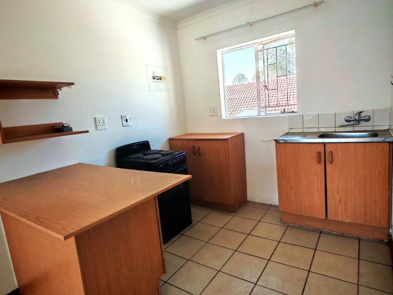 A functional kitchen featuring wood-finish cabinetry, a stainless steel sink, tiled flooring, and a freestanding stove, offering potential for modernization.