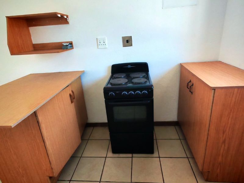 A compact kitchen area featuring wood-finish cabinetry, a freestanding stove, and tiled flooring, requiring minor repairs and cosmetic updates.