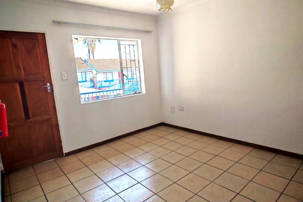 An empty bedroom featuring tiled flooring, a timber door, and a window with security bars, providing a blank canvas for personalization.