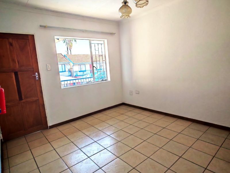 An empty bedroom featuring tiled flooring, a timber door, and a window with security bars, providing a blank canvas for personalization.