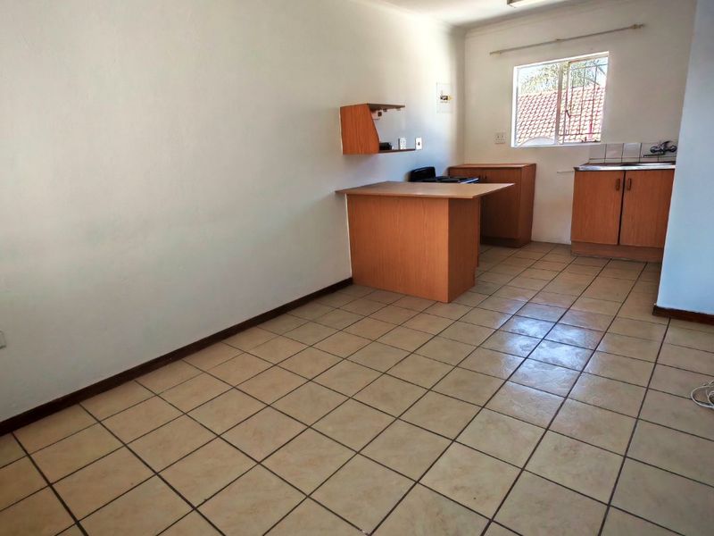 An empty kitchen area featuring tiled flooring, built-in wooden cabinetry, a sink, and a window, offering a functional space ready for modernization.