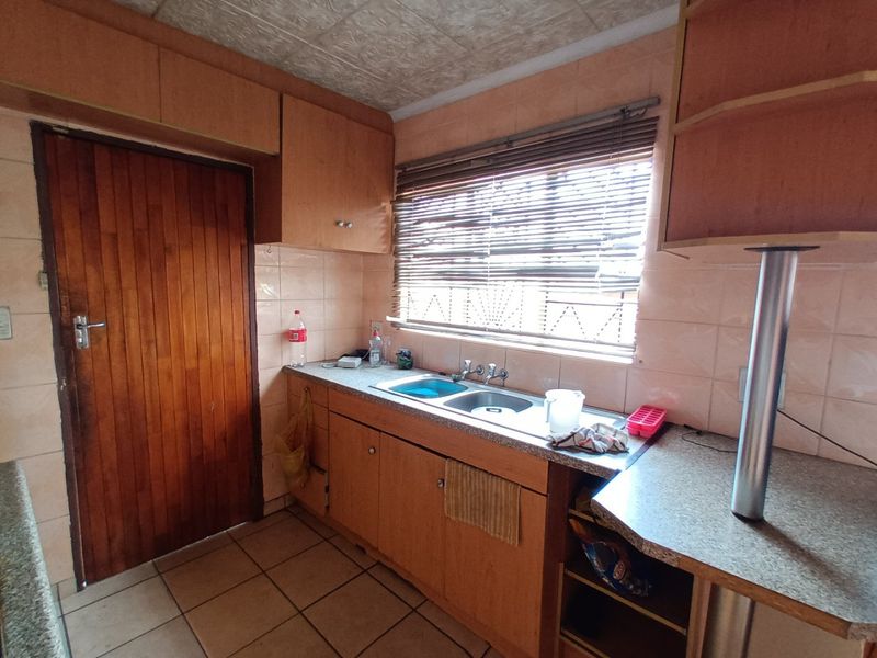 A dated kitchen featuring wooden cabinetry, a double basin sink, tiled backsplash, and tiled flooring, offering potential for a modern renovation.