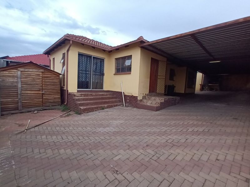 Rear exterior view featuring a paved driveway, large carport, and access steps leading to a sliding glass door entrance.