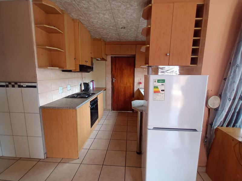 A functional kitchen featuring wooden cabinetry, built-in oven and hob, tiled backsplash, and tiled flooring, offering potential for modernization.