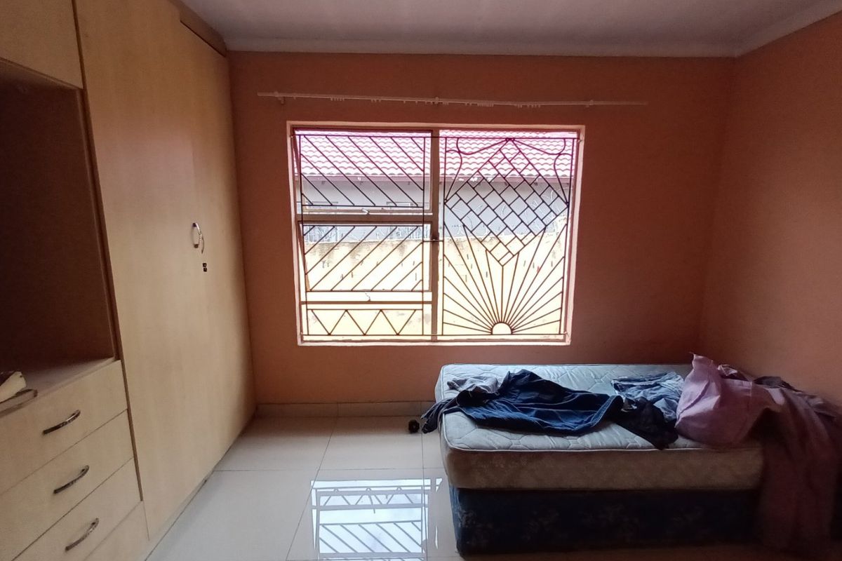 A bedroom featuring tiled flooring, a built-in wardrobe, and a window fitted with security burglar bars.